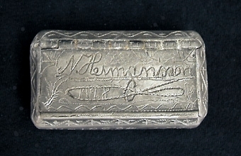 Rektangulär snusdosa med tvärskurna kanter. Full med ristningar, bl.a. N. Hermansson, NH, flera årtal och ornament.