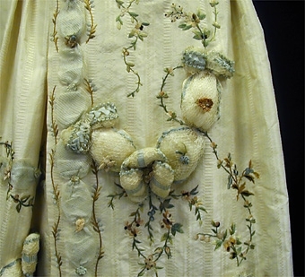Klänning bestående av överklänning (robe) och kjol av enfärgat mönstervävt siden. Broderier av silke samt girlanger av tyll stoppade med bomullsvadd.
Den veckade kjolen, som enbart har broderier mitt fram, har sprund i sidorna och korta kanaler för rynkband.
Överklänningens liv har snörning mitt fram, vilken döljs av en lös slå med klädda knappar. Livet är fodrat med linne samt försett med spröt runt om. En lös, styv sköldformad isättning finns mitt fram under snörningen. 
Ärmarna, som är trekvartslånga, har sydda veck vid armbågarna och en lös nedre del av veckade spetsar. 
Överklänningens kjol är broderad och besatt med girlanger. Släp bak med band på avigsidan för att variera längden.

Klänningen bars första gången av friherrinnan Anne Charlotta von Essen, f. Kruuse af Verchou.
Född 1729 på Klagstorp, Norra Kyrketorp socken, död 1795. Gift 1750 med Ulrik Fredrik von Essen på Kavlås, Hömb socken.