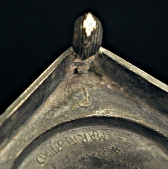 Ljusstake av tenn. Kvadratisk fotplatta med kulor i hörnen. Skaftet balusterformat. Ljushållare med godronnering.