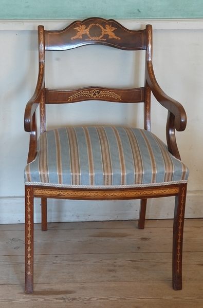 Karmstol med svagt svängda fram och bakben, svängda karmar och svag bakåtsvängd rygg.Två horisontella ryggbrickor med intarsia, även inläggningar i framben, framsarg och ryggstolpar. Stoppad sits med nötfärgat randigt tyg. 1930.