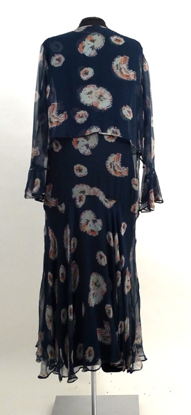 Enligt liggaren: Klänning med jacka. Blåblomig chiffon. Klockad kjol. Liv utan ärm med klockad volang. Tillhörande underklänning, svart crepe de chine. Tillhört Signe Påhlman
