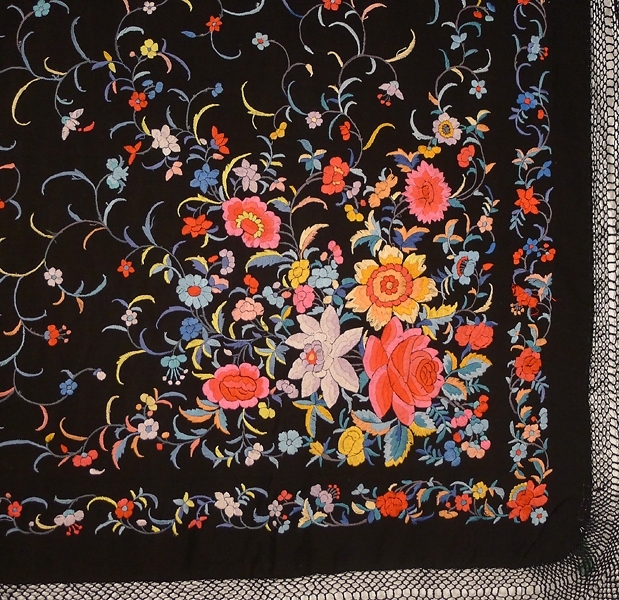 Schal, av svart crepetyg med broderier över hela ytan, i de fyra hörnen större blommönster i flera färger. Lång frans. Möjligen tillverkad i Kina, handgjord. Märkt "85583 FL".