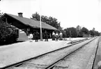 LARS Erik HOLM, f i Överjärna1846, d i Åsbo 1927, var stationsföreståndare i Strålsnäs 1897-1911. Det är sannolikt han som står längt till höger, det kan vara hans hustru, AUGUSTA Christina HOLM f Olsdotter (1844-1935) som står närmast honom.
Flickorna på bilden kan då vara de tre döttrarna, Anna (1875-1960), Lotten (1881-1968) och Karin (1888-1869).
 
År 1900 hade stationen tre anställda.  
Den ljusklädde längst till vänster skulle kunna vara Axel Holm (1885-1948). Han fick anställning som extra kontorist vid stationen 1901, men kan ha arbetat där också dessförinnan, efter avslutad skolgång 1899 eller 1900.