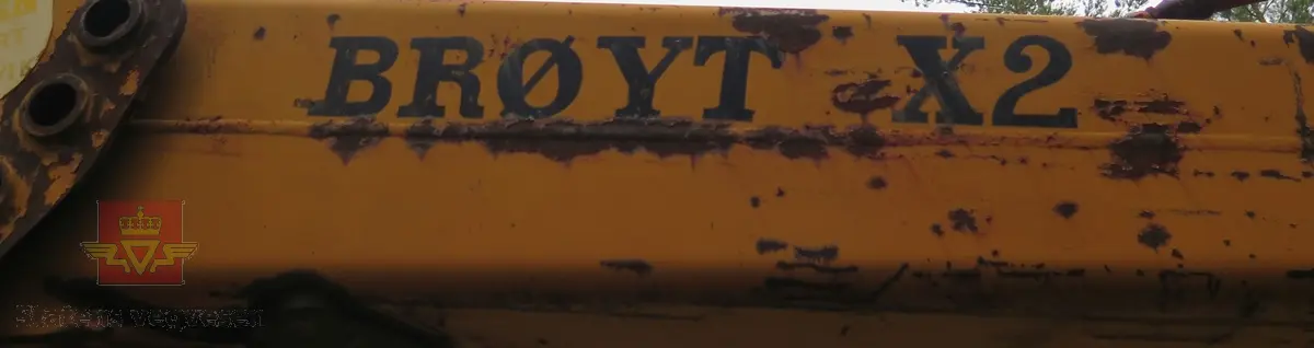 Gravemaskin, hjulgående. 2 jernhjul foran og 2 gummihjul bak. Maskinen er oransje med svart sete. Motoren er en 4-sylindret dieseldrevet type fra Perkins. Gravemaskinen var ikke selvgående, men forflyttet seg med gravearmen under arbeid. Ved transport mellom arbeidsstedene hektet en skuffen i lasteplanet og løftet opp "forhjulene" slik at den ble transportert som en henger.