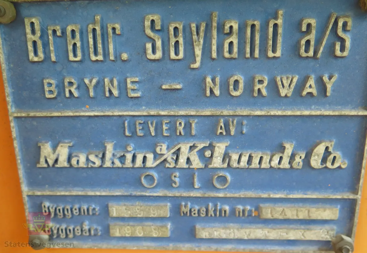 Gravemaskin, hjulgående. 2 jernhjul foran og 2 gummihjul bak. Maskinen er oransje med svart sete. Motoren er en 4-sylindret dieseldrevet type fra Perkins. Gravemaskinen var ikke selvgående, men forflyttet seg med gravearmen under arbeid. Ved transport mellom arbeidsstedene hektet en skuffen i lasteplanet og løftet opp "forhjulene" slik at den ble transportert som en henger.
