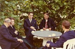 Nokre menn sit rundt eit bord. På bordet et det kaffikoppar.