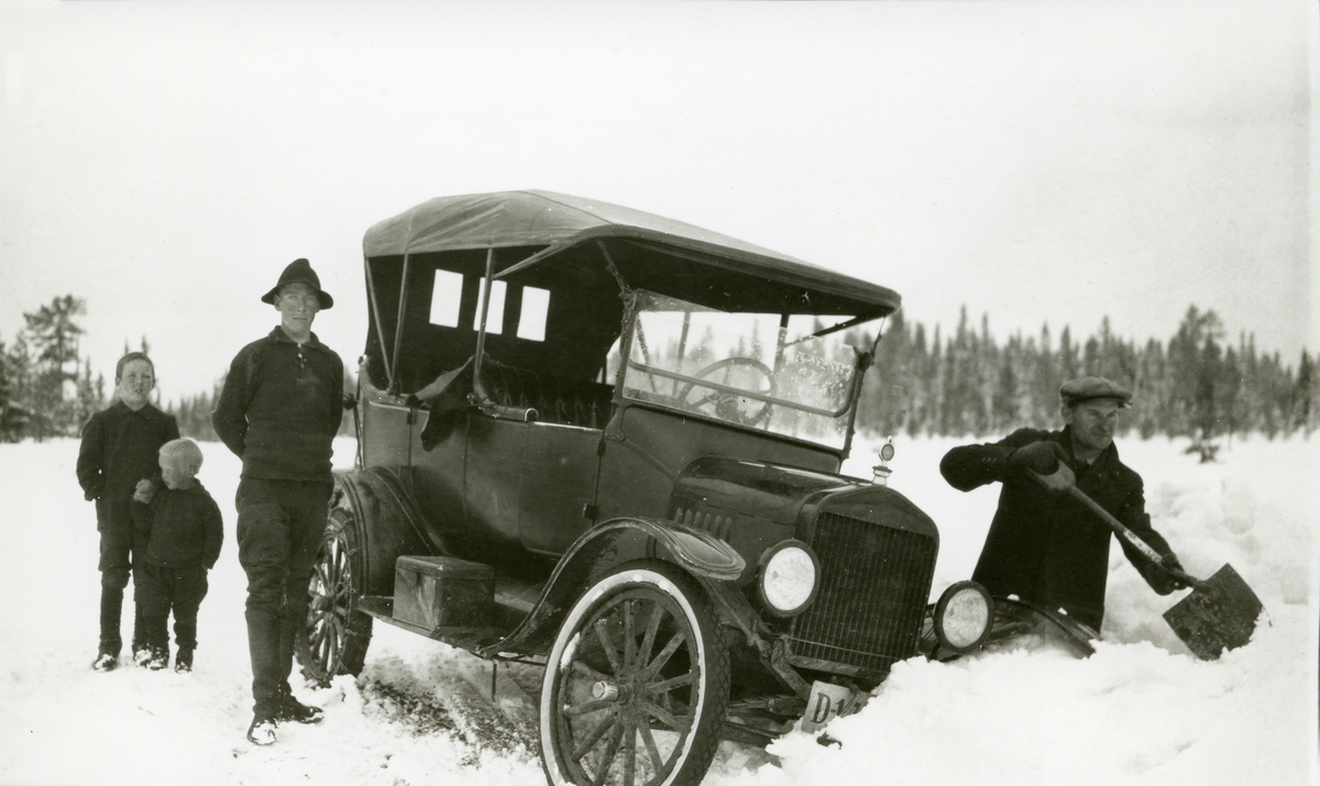 Bil - havnet i grøfta ved Elverumsveien. Mann står og "måkkar" snø for å få bilen opp igjen. Mann og to gutter står til venstre for bilen.