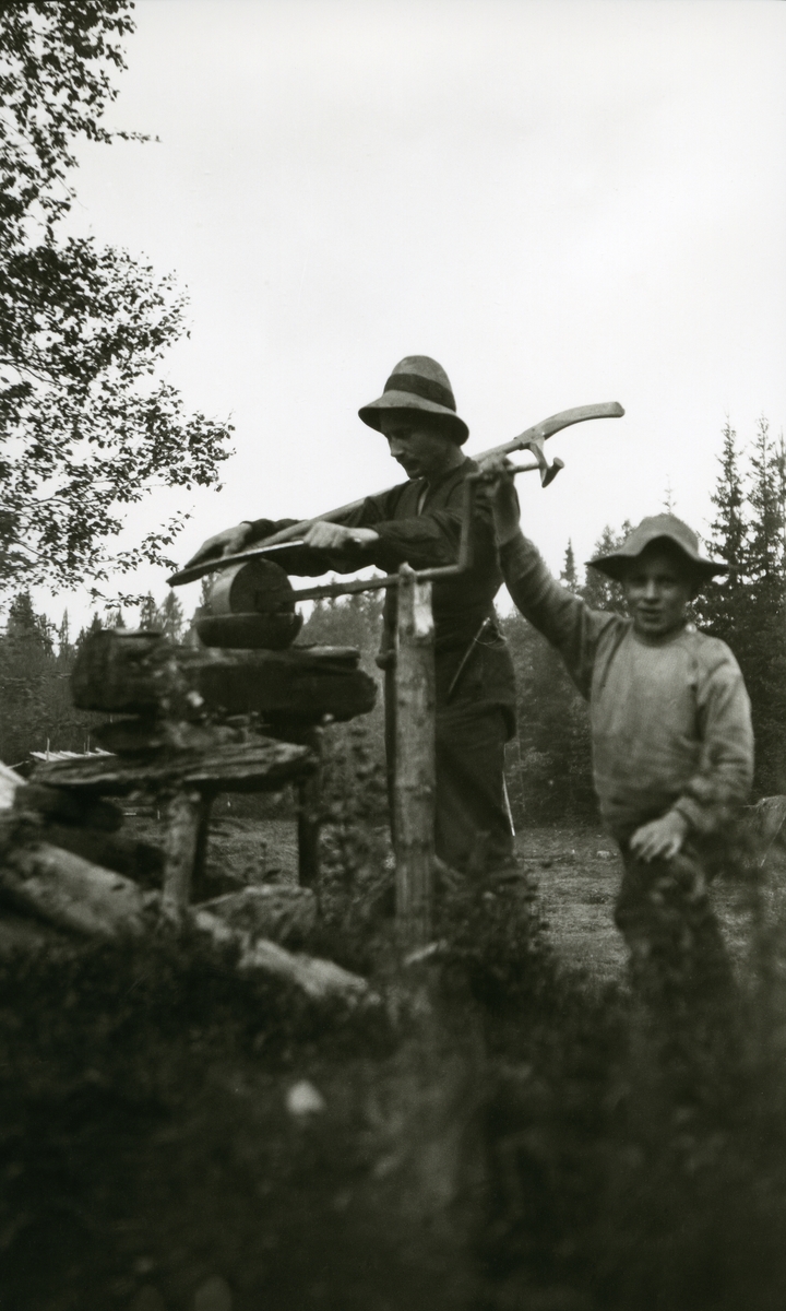 Ingvar Galaasen (3/8  1880) står og sliper ljåen i Galåsen, Karsten Tandåneset (To brødre med samme navn Karsten Oleiv Tannåneset nr 1 født 27.04.1907 død samme år, nr 2 født 20.12.1908 død 2010) drar slipesteinen.