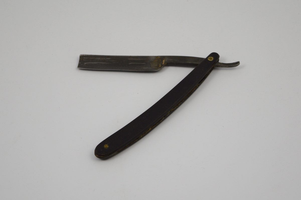 Sammenleggbar barberkniv med rett egg. Knivbladet har konisk tverrsnitt. Bladet munner ut i tynt skaft
med en krumning som holdegrep med fingeren. Skaftet er naglet fast til
kniven. Består av to deler som fungerer som beskyttelse i sammenlagt
stilling.