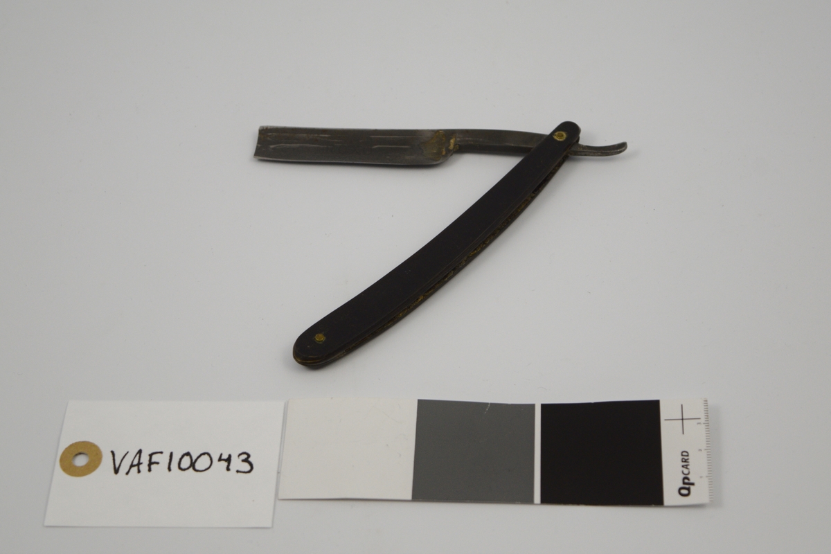 Sammenleggbar barberkniv med rett egg. Knivbladet har konisk tverrsnitt. Bladet munner ut i tynt skaft
med en krumning som holdegrep med fingeren. Skaftet er naglet fast til
kniven. Består av to deler som fungerer som beskyttelse i sammenlagt
stilling.