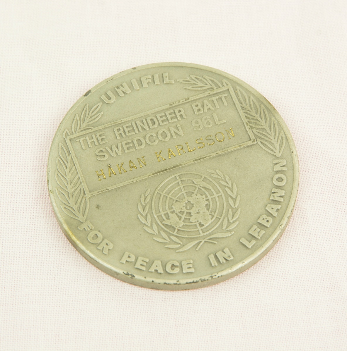 Medalj i metall från FN-insatsen i Libanon. På ena sidan av medaljen finns en FN logga omgiven av en lagerkrans, under står "UNIFIL FOR PEACE IN LEBANON" ovanför finns ett textfält med texten "THE REINDEER BATT SWEDCON 96L HÅKAN KARLSSON". På andra sidan finns en karta över Libanons västra del samt delar av Israel och Syrien.