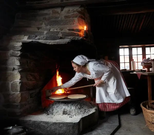 Lefsebakst i Numedalstunet på Norsk Folkemuseum. En kvinne i tradisjonell drakt steker lefser over åpen ild i en grue, en del av norsk matkultur.