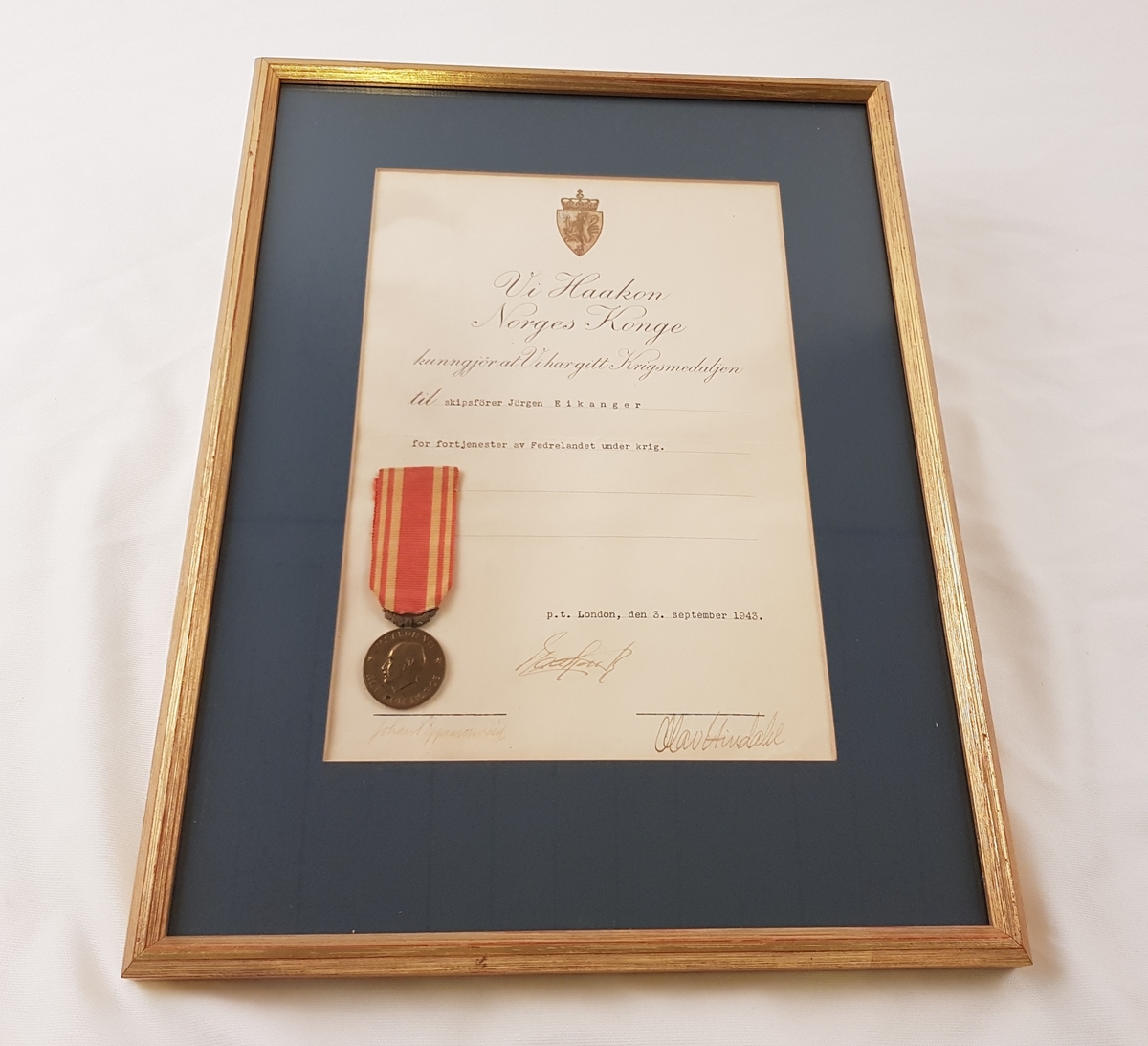 Krigsmedalje med tilhørende diplom satt i ramme med glass.