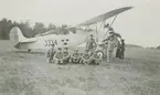 Grupporträtt av militärer framför spaningsflygplan S 6 på flygfältet Wisborgs slätt, 1929. Flygplanet märkt nummer 3334. Flygmekaniker i bakgrunden.