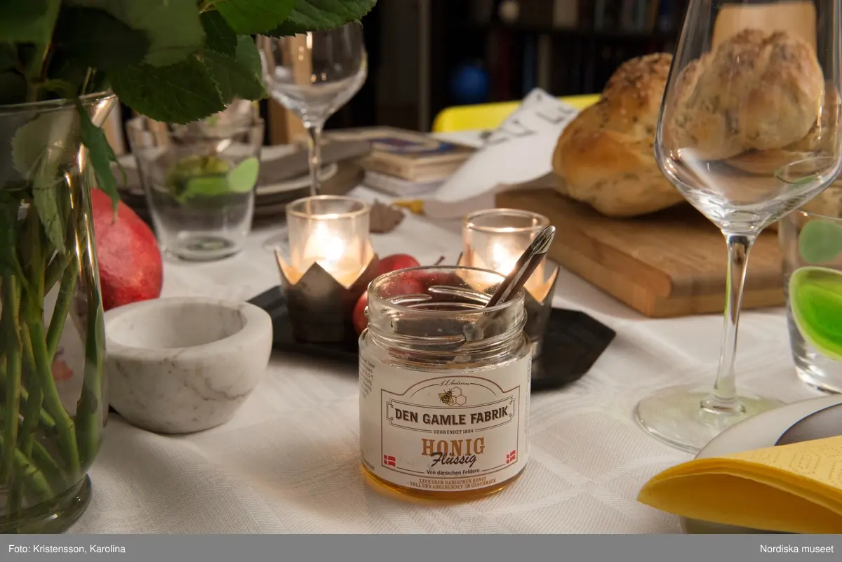 Rosh Hashana. Maten på ett judiskt nyårsbord: granatäpple, honung, bröd, äppelskivor, hummus, aubergine- och tomatröra, I köket: köttgryta (Hammin??) med sötpotatis, blomkål med citron, kycklingklubbor, ingefärssoppa, kryddris med linser och russin.