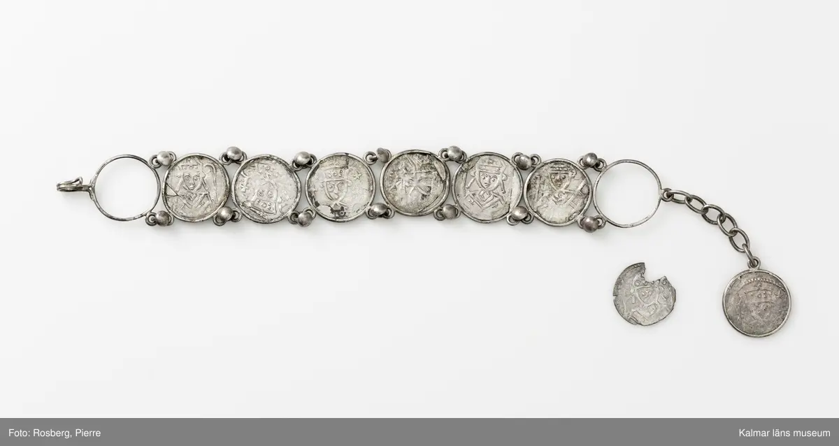 KLM 14507 Myntfynd, ett armband, bildat av silvermynt. Armbandet består av åtta infällda mynt, varav ett har lossnat från sin inramning. Mynt från Valdemar I:s tid, samt ärkebiskop Absalon, 1100-talets slut. Mynten i armbandet härstammar från ett jordfynd av ca 30 stycken likadana mynt, hittade i jorden på Åby prästgårds ägor omkr 1885. Av de nu befintliga åtta stycken, är präglade för Knut VI, Lund