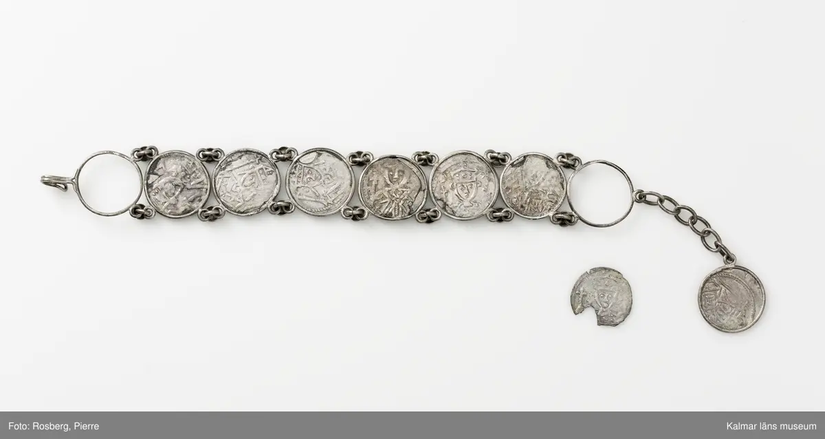 KLM 14507 Myntfynd, ett armband, bildat av silvermynt. Armbandet består av åtta infällda mynt, varav ett har lossnat från sin inramning. Mynt från Valdemar I:s tid, samt ärkebiskop Absalon, 1100-talets slut. Mynten i armbandet härstammar från ett jordfynd av ca 30 stycken likadana mynt, hittade i jorden på Åby prästgårds ägor omkr 1885. Av de nu befintliga åtta stycken, är präglade för Knut VI, Lund