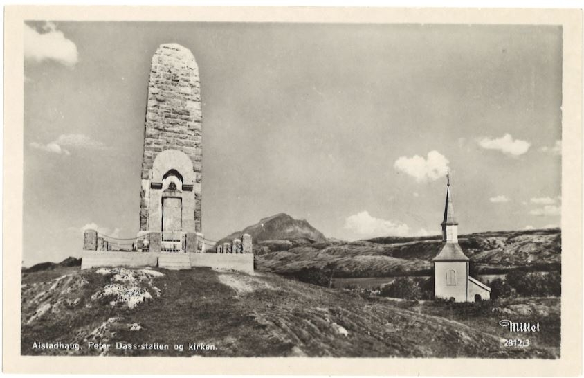 Svart/hvitt foto med hvit kant. Bautaen over Petter Dass med Alstahaug kirke og Vettfjellet i bakgrunnen.