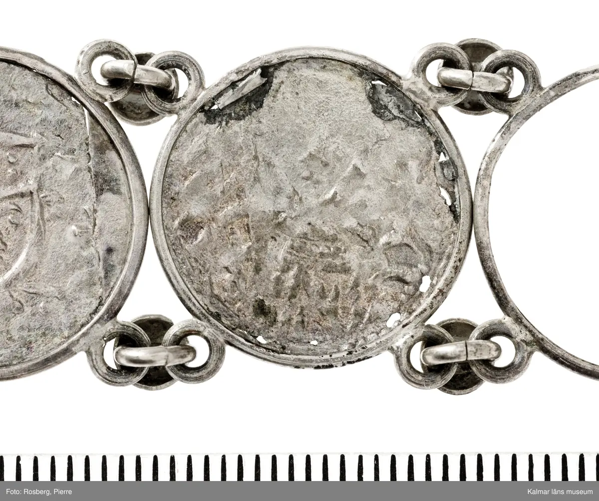 KLM 14507 Myntfynd, ett armband, bildat av silvermynt. Armbandet består av åtta infällda mynt, varav ett har lossnat från sin inramning. Mynt från Valdemar I:s tid, samt ärkebiskop Absalon, 1100-talets slut. Mynten i armbandet härstammar från ett jordfynd av ca 30 stycken likadana mynt, hittade i jorden på Åby prästgårds ägor omkr 1885. Av de nu befintliga åtta stycken, är präglade för Knut VI, Lund