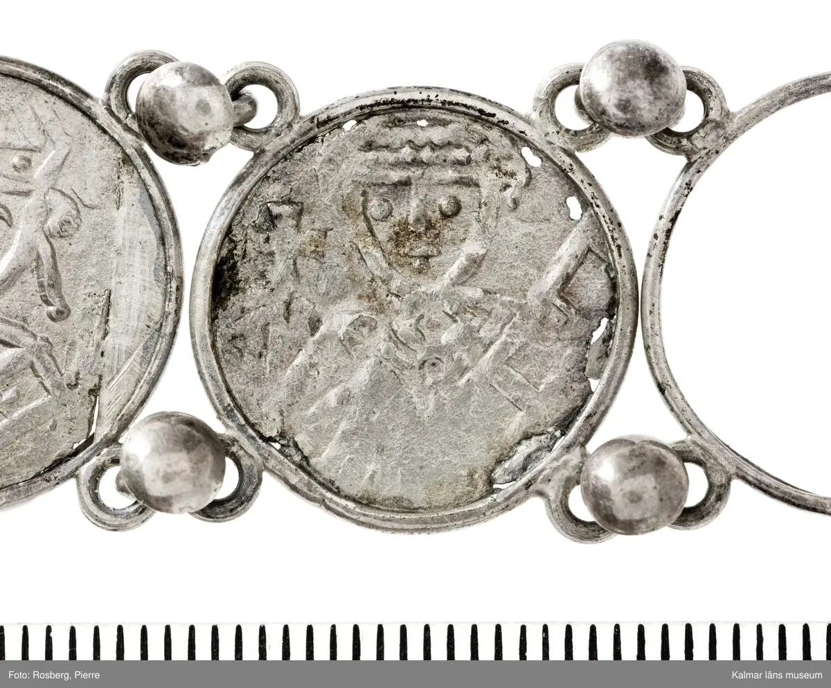 KLM 14507 Myntfynd, ett armband, bildat av silvermynt. Armbandet består av åtta infällda mynt, varav ett har lossnat från sin inramning. Mynt från Valdemar I:s tid, samt ärkebiskop Absalon, 1100-talets slut. Mynten i armbandet härstammar från ett jordfynd av ca 30 stycken likadana mynt, hittade i jorden på Åby prästgårds ägor omkr 1885. Av de nu befintliga åtta stycken, är präglade för Knut VI, Lund