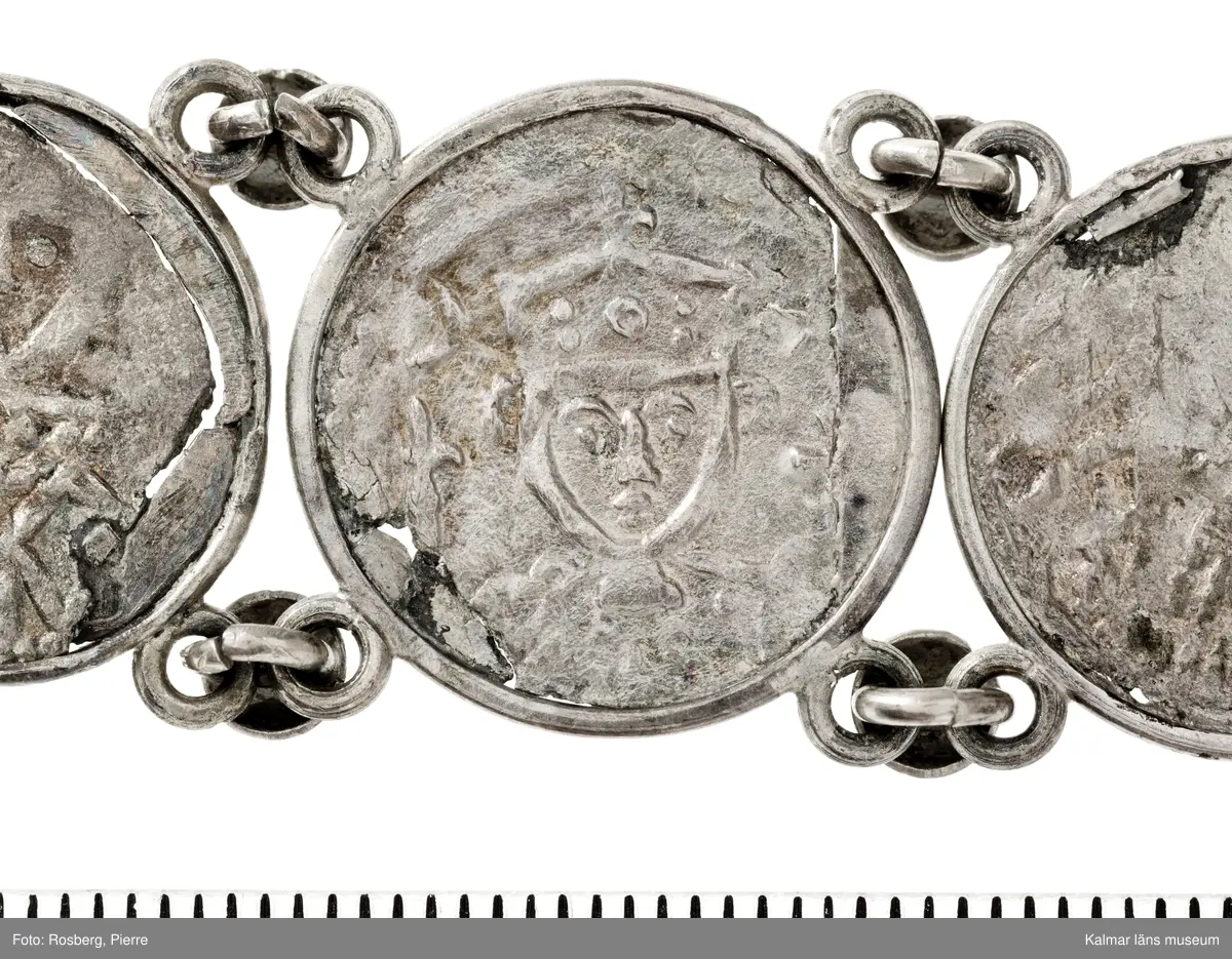 KLM 14507 Myntfynd, ett armband, bildat av silvermynt. Armbandet består av åtta infällda mynt, varav ett har lossnat från sin inramning. Mynt från Valdemar I:s tid, samt ärkebiskop Absalon, 1100-talets slut. Mynten i armbandet härstammar från ett jordfynd av ca 30 stycken likadana mynt, hittade i jorden på Åby prästgårds ägor omkr 1885. Av de nu befintliga åtta stycken, är präglade för Knut VI, Lund