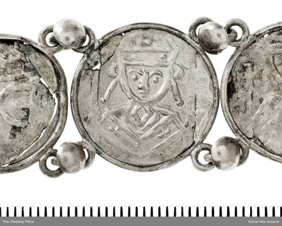 KLM 14507 Myntfynd, ett armband, bildat av silvermynt. Armbandet består av åtta infällda mynt, varav ett har lossnat från sin inramning. Mynt från Valdemar I:s tid, samt ärkebiskop Absalon, 1100-talets slut. Mynten i armbandet härstammar från ett jordfynd av ca 30 stycken likadana mynt, hittade i jorden på Åby prästgårds ägor omkr 1885. Av de nu befintliga åtta stycken, är präglade för Knut VI, Lund