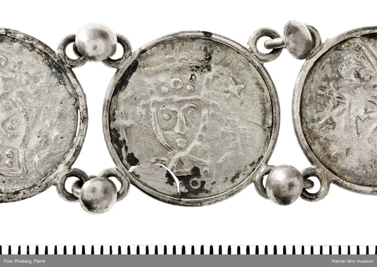 KLM 14507 Myntfynd, ett armband, bildat av silvermynt. Armbandet består av åtta infällda mynt, varav ett har lossnat från sin inramning. Mynt från Valdemar I:s tid, samt ärkebiskop Absalon, 1100-talets slut. Mynten i armbandet härstammar från ett jordfynd av ca 30 stycken likadana mynt, hittade i jorden på Åby prästgårds ägor omkr 1885. Av de nu befintliga åtta stycken, är präglade för Knut VI, Lund