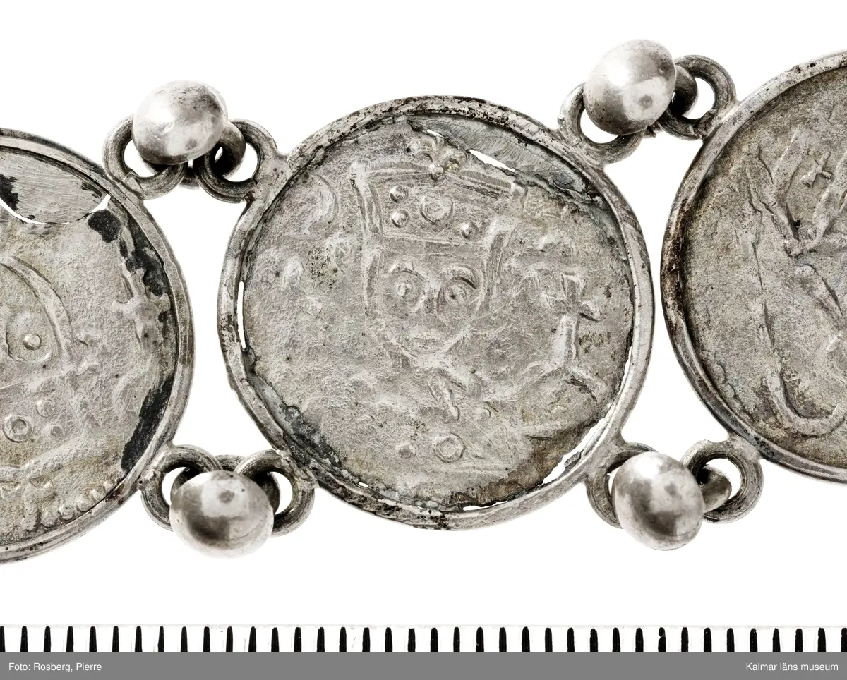 KLM 14507 Myntfynd, ett armband, bildat av silvermynt. Armbandet består av åtta infällda mynt, varav ett har lossnat från sin inramning. Mynt från Valdemar I:s tid, samt ärkebiskop Absalon, 1100-talets slut. Mynten i armbandet härstammar från ett jordfynd av ca 30 stycken likadana mynt, hittade i jorden på Åby prästgårds ägor omkr 1885. Av de nu befintliga åtta stycken, är präglade för Knut VI, Lund