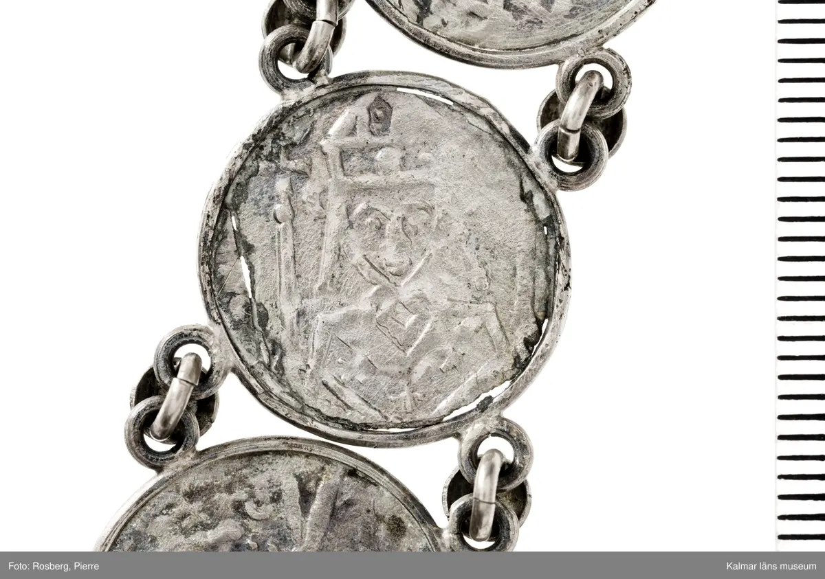 KLM 14507 Myntfynd, ett armband, bildat av silvermynt. Armbandet består av åtta infällda mynt, varav ett har lossnat från sin inramning. Mynt från Valdemar I:s tid, samt ärkebiskop Absalon, 1100-talets slut. Mynten i armbandet härstammar från ett jordfynd av ca 30 stycken likadana mynt, hittade i jorden på Åby prästgårds ägor omkr 1885. Av de nu befintliga åtta stycken, är präglade för Knut VI, Lund