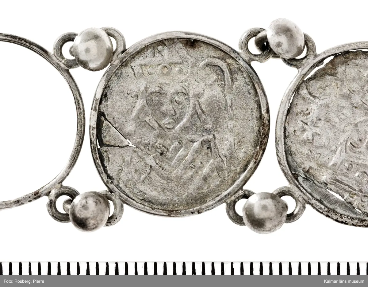 KLM 14507 Myntfynd, ett armband, bildat av silvermynt. Armbandet består av åtta infällda mynt, varav ett har lossnat från sin inramning. Mynt från Valdemar I:s tid, samt ärkebiskop Absalon, 1100-talets slut. Mynten i armbandet härstammar från ett jordfynd av ca 30 stycken likadana mynt, hittade i jorden på Åby prästgårds ägor omkr 1885. Av de nu befintliga åtta stycken, är präglade för Knut VI, Lund