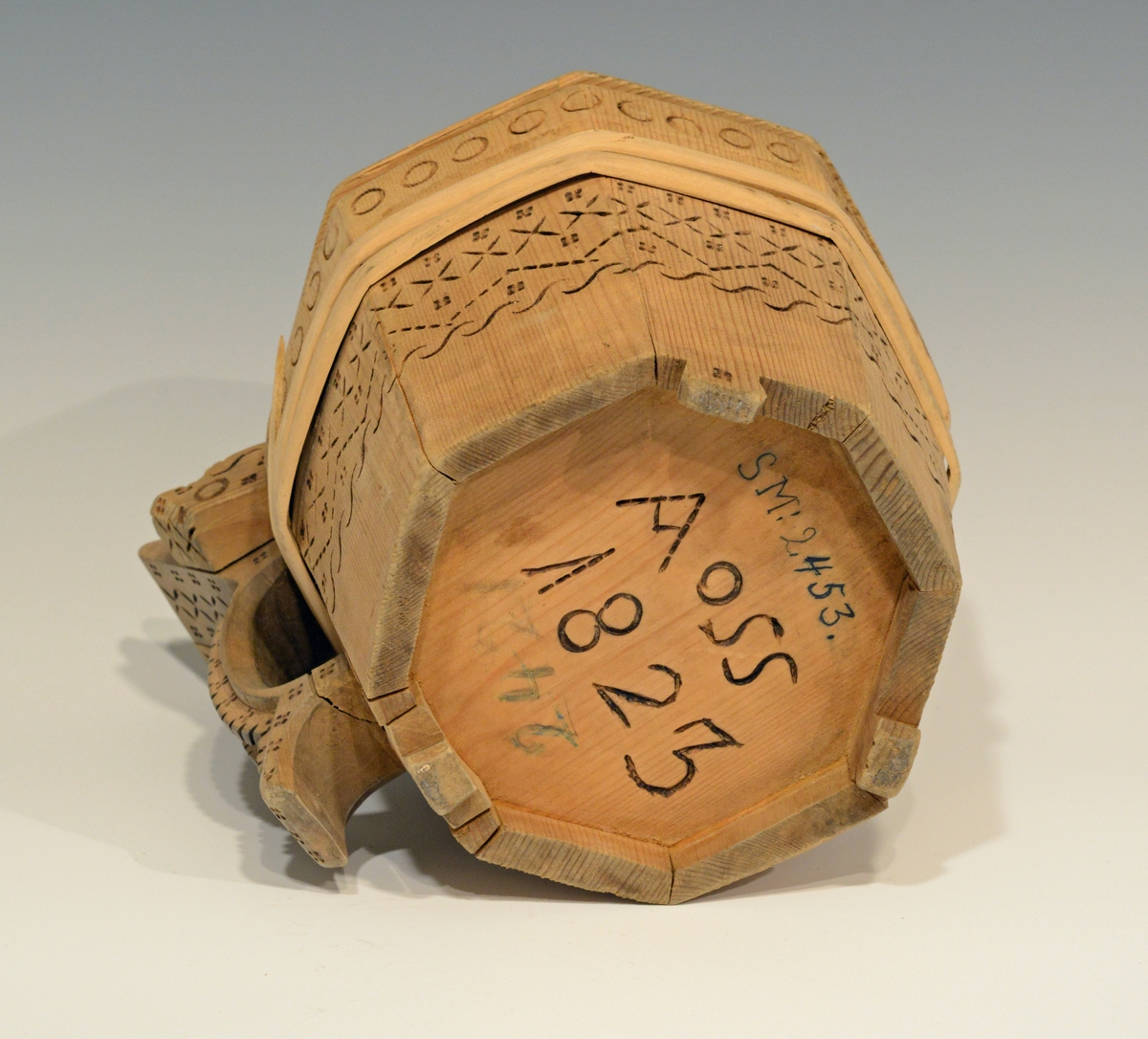 Fra katalog: Ottekantet smørkande og stav med hank og laak og tre smaa føtter, utvendig svimerket og en slynget ring oppe paa laaket, indvendig
rik rosette. Under staar brændemerket: A OSS 1823,