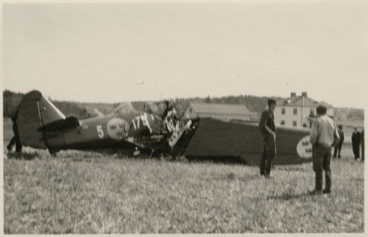 Havererat militärt skolflygplan SK 14 nummer 675, märkt F 5-175 på ett fält utanför Vittsäter, sydost om Nykil i Östergötland, den 30 april 1940. Män i närheten av flygplanet. Serie om 8 bilder.