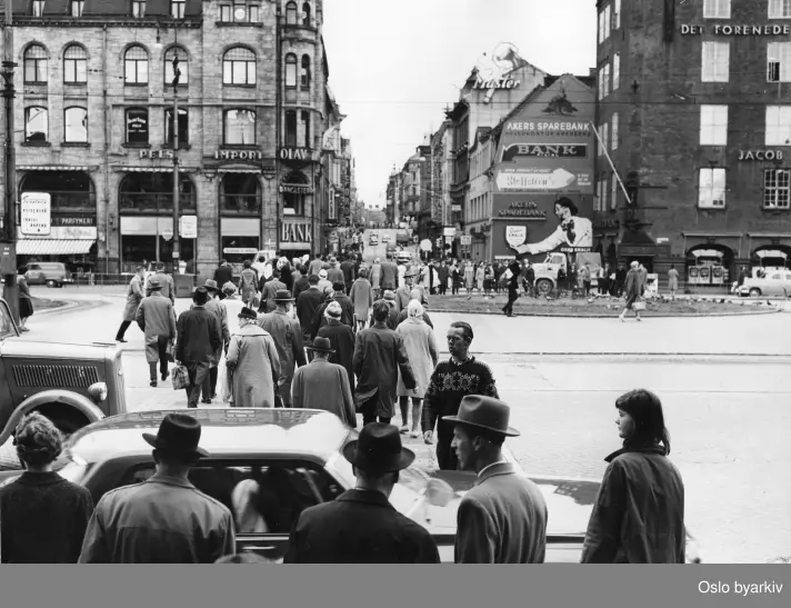 Folk på vei ut fra Østbanen. Fotografen har stått på stasjonstrappa og sett over Jernbarnetorget og oppover Karl Johans gate