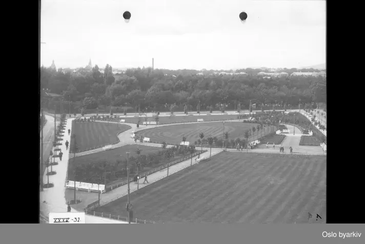 Oversiktsbilde over parken (ferdig i 1922) med gangveier, parkbenker, plener og beplantning. Uelandsgata opp i bakgrunnen. Kierschows gate nede til venstre. Bildet tatt fra kirken mot Nordre Gravlund. Albumtittel: Gråbeinsletta og anlegg ved Sagene kirke, Grev Wedels plass, Grønland