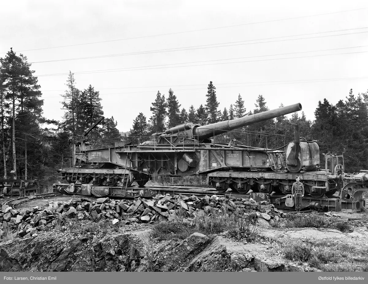 Kanon på jernbanevogn, batteriet på Knatterud, Varteig ved Sarpsborg 1945. De to jernbanekanonene ble forsøkt plassert på to fundamenter på Strand gård i daværende Onsøy kommune fra høsten 1942, for å beskytte Fredrikstad havn. Det ene fundamentet ble for dårlig pga kvikkleire, og høsten 1943 ble kanonene flyttet til Knatterud. 
Soldat, ukjent.
Deutsche Reichsbahn, Berlin.

Dette er en "28 cm kanon Schwere Bruno" Den hadde en totallengde på 22.8 meter og en vekt på 118 tonn. Lengden på kanonrøret 11.93 meter. 
Utgangshastighet på granaten var 860 m/sek. Maks skuddvidde 37.8 km. Skuddhastighet ca 10 skudd i timen.  
Kilde: Østfold Historielags tidsskrift WIWAR nr1 2002.