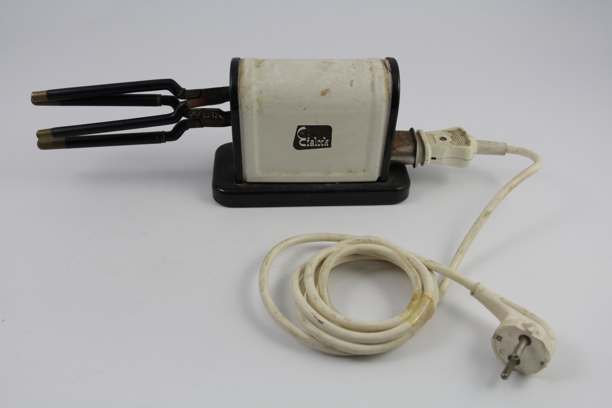 Eletrisk krølltang bestående av fire deler:
a-b) krølltenger: 2 stk. sylindriske håndtak (a kan beveges).  Når håndtakene føres sammen, presses sylinder i andre enden ned i hul del. 
c) elektrisk varmeapparat, uttak støpsel og ledning på den ene siden. Rektangulær sokkel. Påsatt rektangulær del med avrundet overside. Kortside: inntak for to krølltenger. Oval åpning. 
d) Ledning med kontakter.