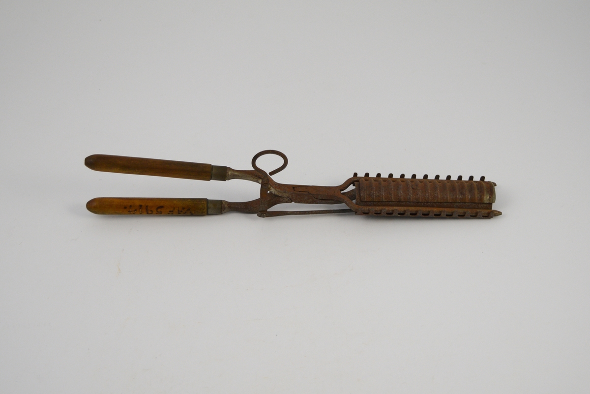 Krølltang: To jern som krysser hverandre i et hengslingsparti, og hvor den ene stang er stukket gjennom den andre. Sammenhengslingen er klinket. Det ene "jern" har to runde tynne tinder stående i spiss u-form og med butte ender. Det andre "jern" består av to deler, en fast og en bevegelig. Den flat utformede og avkuttede "arm" er festet med to nagler til et krumbøyd stykke lettmetall med 12 rett oppstående tagger på hver side. På oversiden av det krumbøyde lettmetall er lagt et 3 cm bredt rektangulært stykke lettmetall med tversgående rifler. Det riflete lettmetallstykket er bevegelig innenfor et rektangulært felt (hull), på undersiden av det andre lettmetallstykket, og hvor det er naglet fast til en bevegelig "arm". Denne "arm" består av to sammen-naglete deler stående vinkelrett på hverandre, den korte del avsluttes med en bøyd krok for fingergrep. Håndtakene dreiet med avrundet spiss i den ene enden, to metallringer markerer overgangen til jernene.