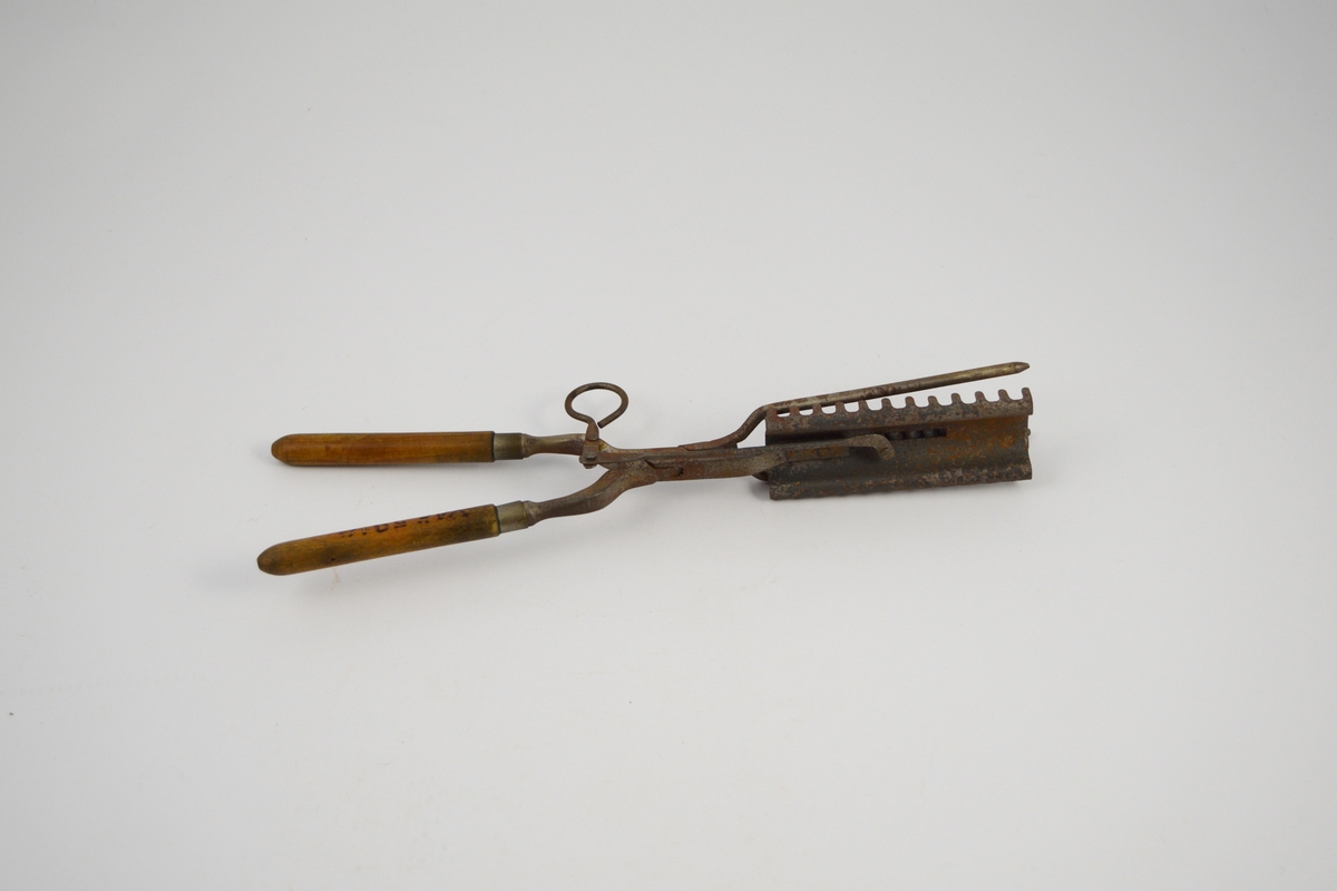 Krølltang: To jern som krysser hverandre i et hengslingsparti, og hvor den ene stang er stukket gjennom den andre. Sammenhengslingen er klinket. Det ene "jern" har to runde tynne tinder stående i spiss u-form og med butte ender. Det andre "jern" består av to deler, en fast og en bevegelig. Den flat utformede og avkuttede "arm" er festet med to nagler til et krumbøyd stykke lettmetall med 12 rett oppstående tagger på hver side. På oversiden av det krumbøyde lettmetall er lagt et 3 cm bredt rektangulært stykke lettmetall med tversgående rifler. Det riflete lettmetallstykket er bevegelig innenfor et rektangulært felt (hull), på undersiden av det andre lettmetallstykket, og hvor det er naglet fast til en bevegelig "arm". Denne "arm" består av to sammen-naglete deler stående vinkelrett på hverandre, den korte del avsluttes med en bøyd krok for fingergrep. Håndtakene dreiet med avrundet spiss i den ene enden, to metallringer markerer overgangen til jernene.