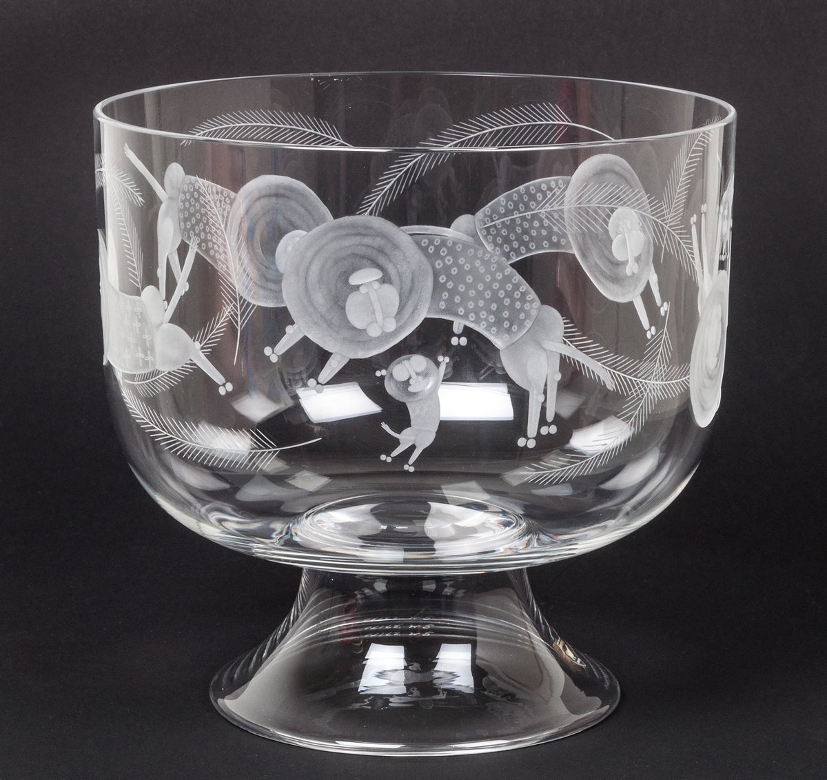 Skål på fot, kristall. Orrefors glasbruk, desing Gunnar Cyrén. Cylindrisk med välvd botten. Konkav fot. Graverad dekor av lejon och apor. På foten grå sköldformad etikett med i vitt orre och texten : ORREFORS SWEDEN.