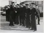 En grupp värnpliktiga står på rad på gårdsplanen framför kasernbyggnader och tar emot medaljer av officerare.