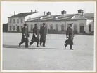 En konteramiral och tre kommendörkaptener går över Sparres kaserngård. I bakgrunden syns bataljonens excercishus.