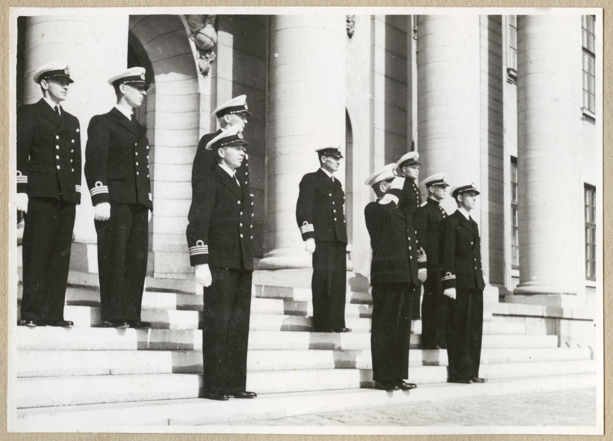 Uniformsklädda militärer av hög rang från marinen och amfibekåren står på trappan till Karlskrona rådhus. Bland annat syns kommendörkaptener, kaptener och löjtnanter. I mitten i den främre raden står konteramiral Ehrensvärd och gör honör.