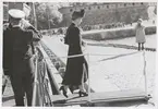 Drottning Louise klivet av en båt vid Kungsbron i Karlskrona. I bakgrunden syns Bastion Aurora. Framför den står en folksamling och några bilar. En uniformsklädd sjöman ombord på fartyget gör honnör.