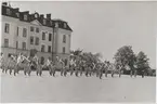 Lottor står med Svenska flaggor på kaserngården på Gräsvik, framför Gräsviks Kanslihus.