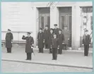 Konteramiral Samuelson ger honnör framför en grupp högre officerare som står givakt framför en portik. Samtliga bär flottans uniformer.