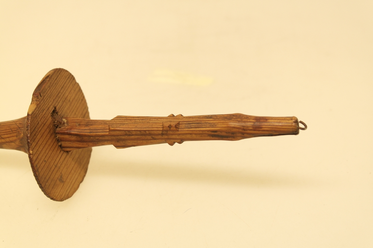 Håndtein i skåret og pusset furu. En lang pinne (tein) med en sirkelrund plate (håndteinsnelle) på midten. Platen er festet ved hjelp av en liten pinne som er tappet gjennom teinpinnen. Den ene enden har utskjæringer og påsatt en liten jernkrok. Den andre enden har en utsparing.