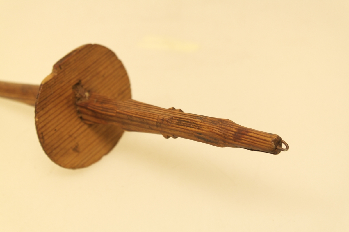 Håndtein i skåret og pusset furu. En lang pinne (tein) med en sirkelrund plate (håndteinsnelle) på midten. Platen er festet ved hjelp av en liten pinne som er tappet gjennom teinpinnen. Den ene enden har utskjæringer og påsatt en liten jernkrok. Den andre enden har en utsparing.