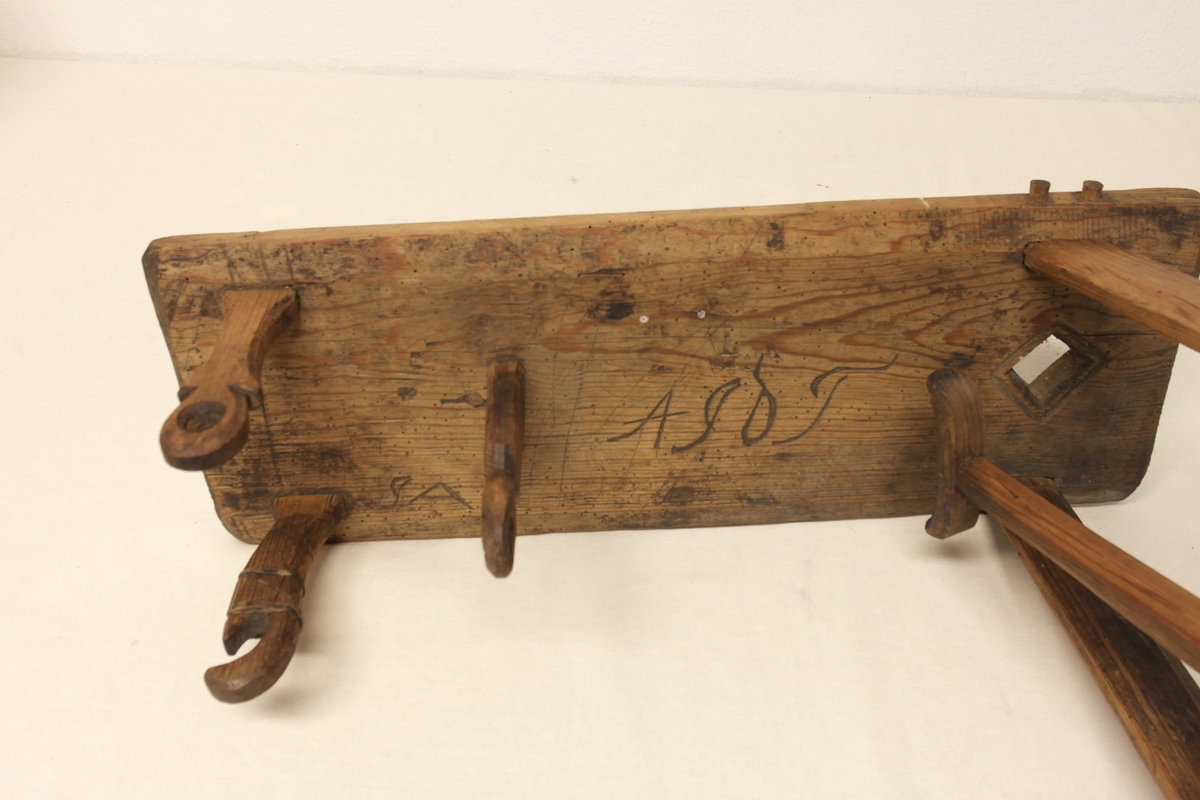 Garnvinde i tre. Stativ festet på ei plate (a). På stativet er det to pinner i kryss (b) som er roterbart ved hjelp av ei sveiv. Det er inngravert initialer og tall i plata, både på oversiden og undersiden.