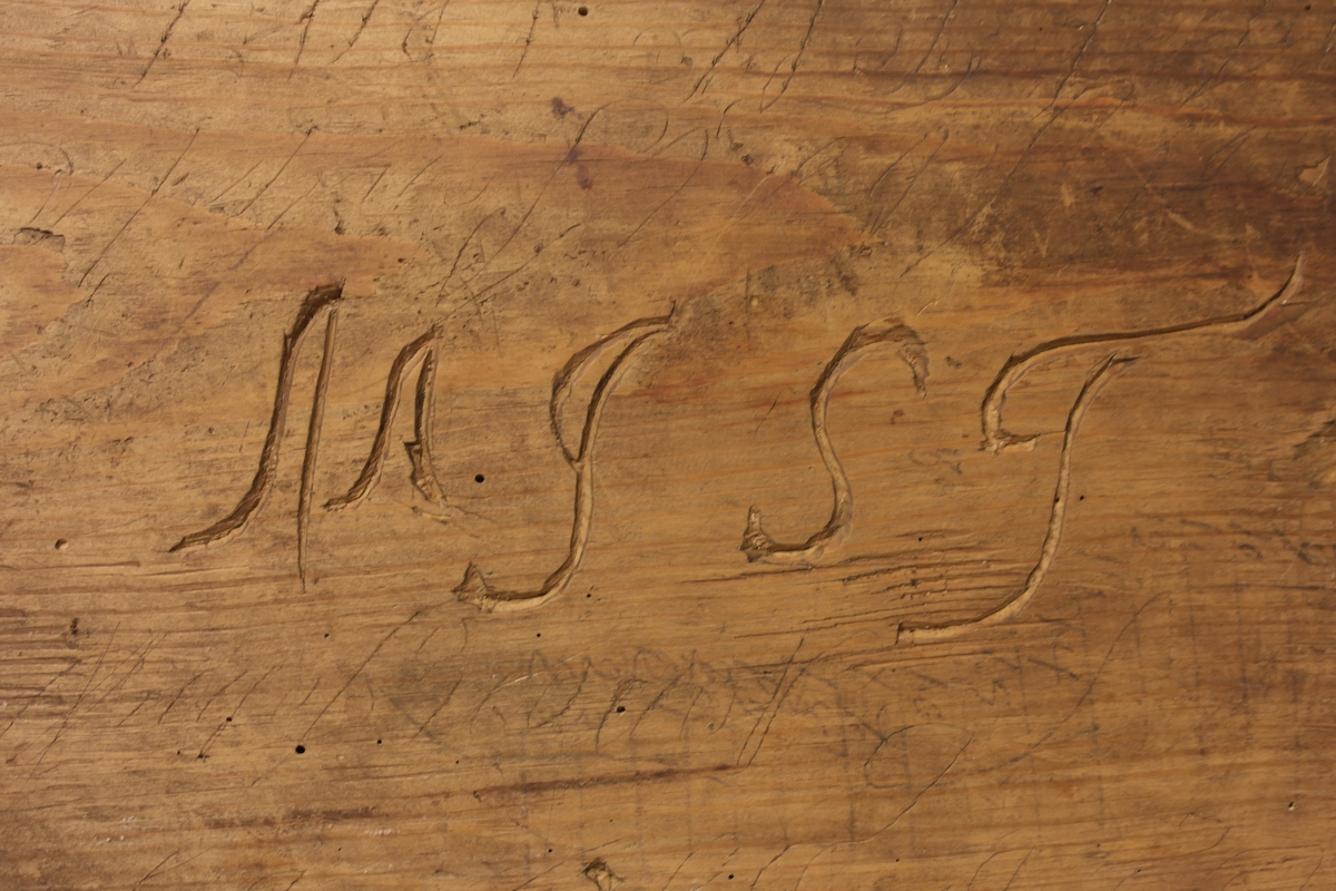 Garnvinde i tre. Stativ festet på ei plate (a). På stativet er det to pinner i kryss (b) som er roterbart ved hjelp av ei sveiv. Det er inngravert initialer og tall i plata, både på oversiden og undersiden.