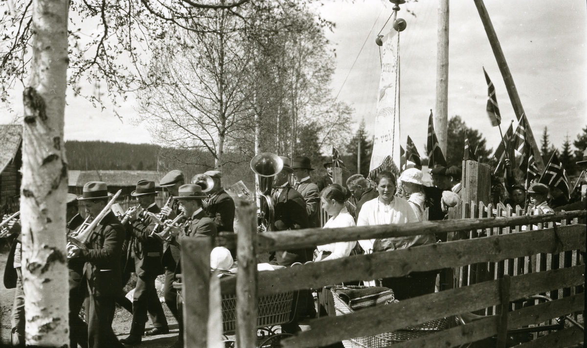 17. mai-tog med hornmusikken på Østby i spissen. Fra venstre: 1) Arve Johansen Haugen (18/11 1891 - 1961) 2) Otto Johansen Haugen (21/8 1897 - 1952) 3) Ole Johansen Haugen (11/11 1878 - 1959) 4) Reidar Østmoe (1903 - 1968) 5) Magnus Johansen Haugen (12/8 1889 - 1961) 6) Helmer J. Bæk (26/1 1870 - 1947) 7) (han med tubaen) Gunnar Bjørseth (17/10 1904 - 1982). Kvinnen under fanen som ser hit: Paula Hemstad g. Ås (1905)